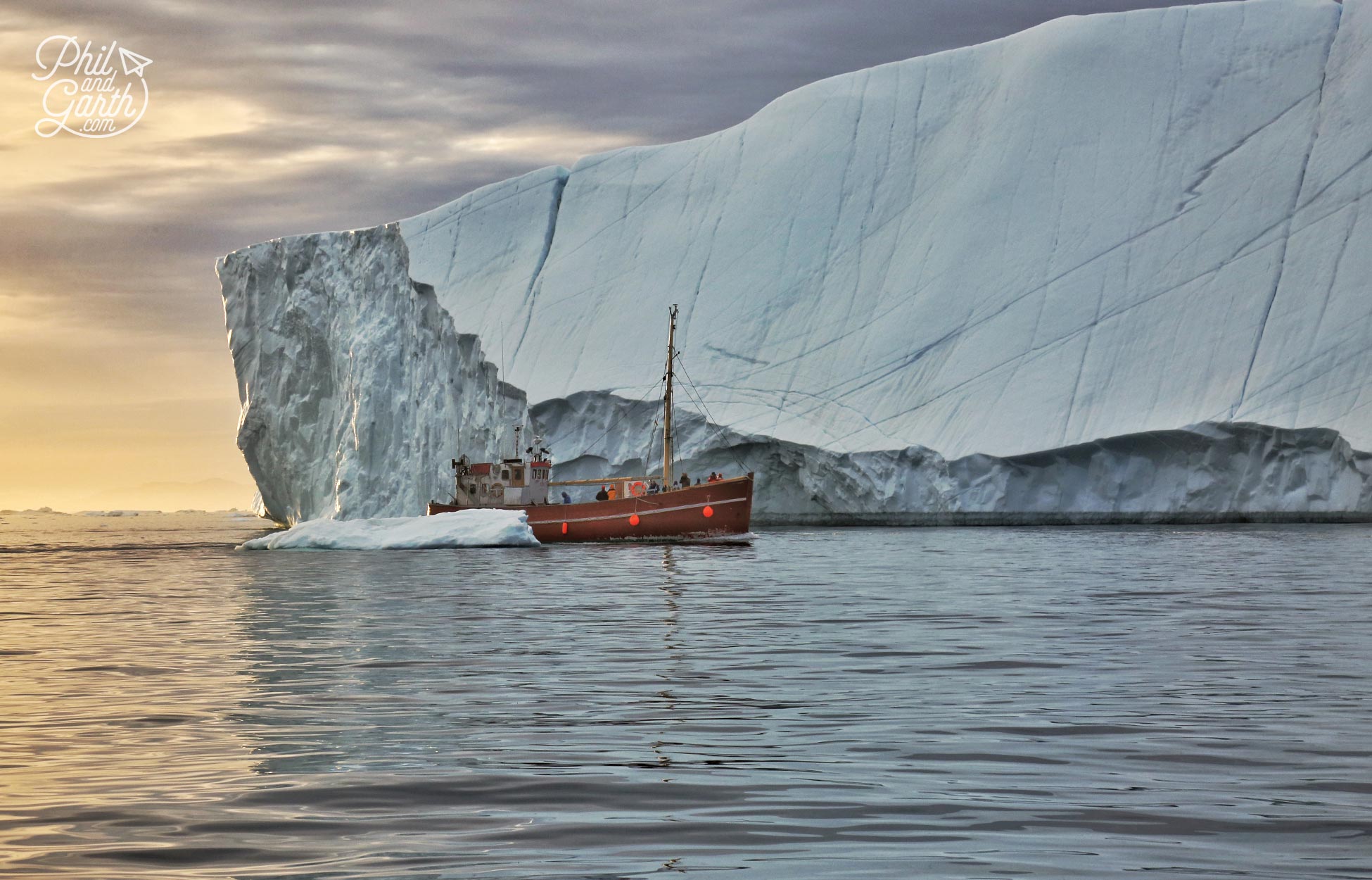 A fishing boat passes icebergs in the midnight sun