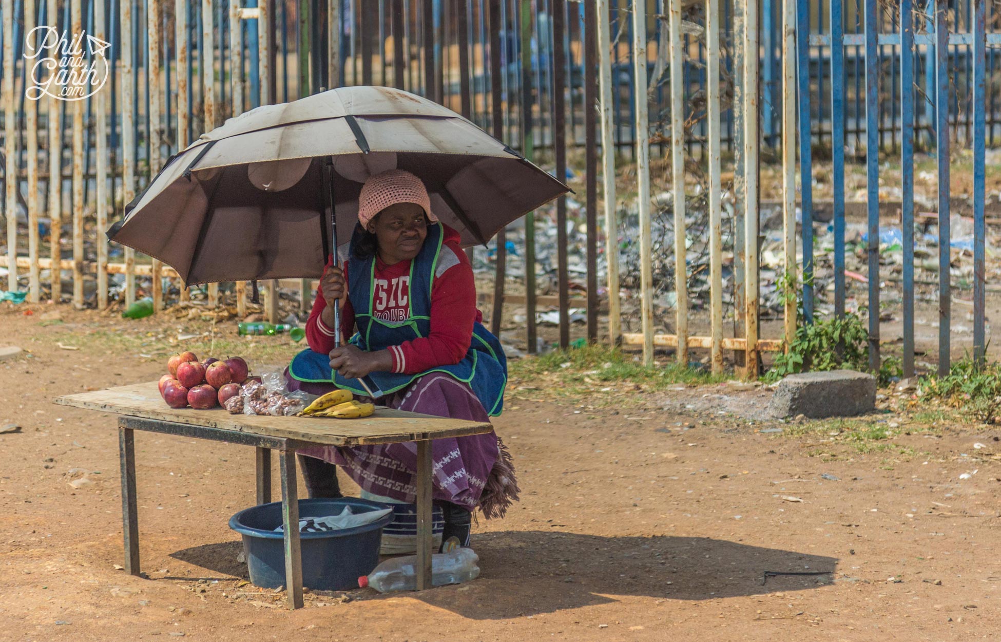 A lady sells a small amount of bananas, apples and nuts