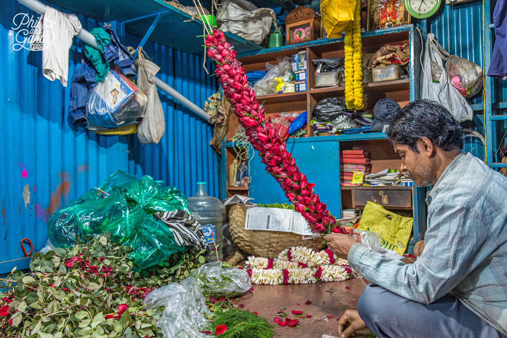 This man threads little red roses together to create somekind of garland