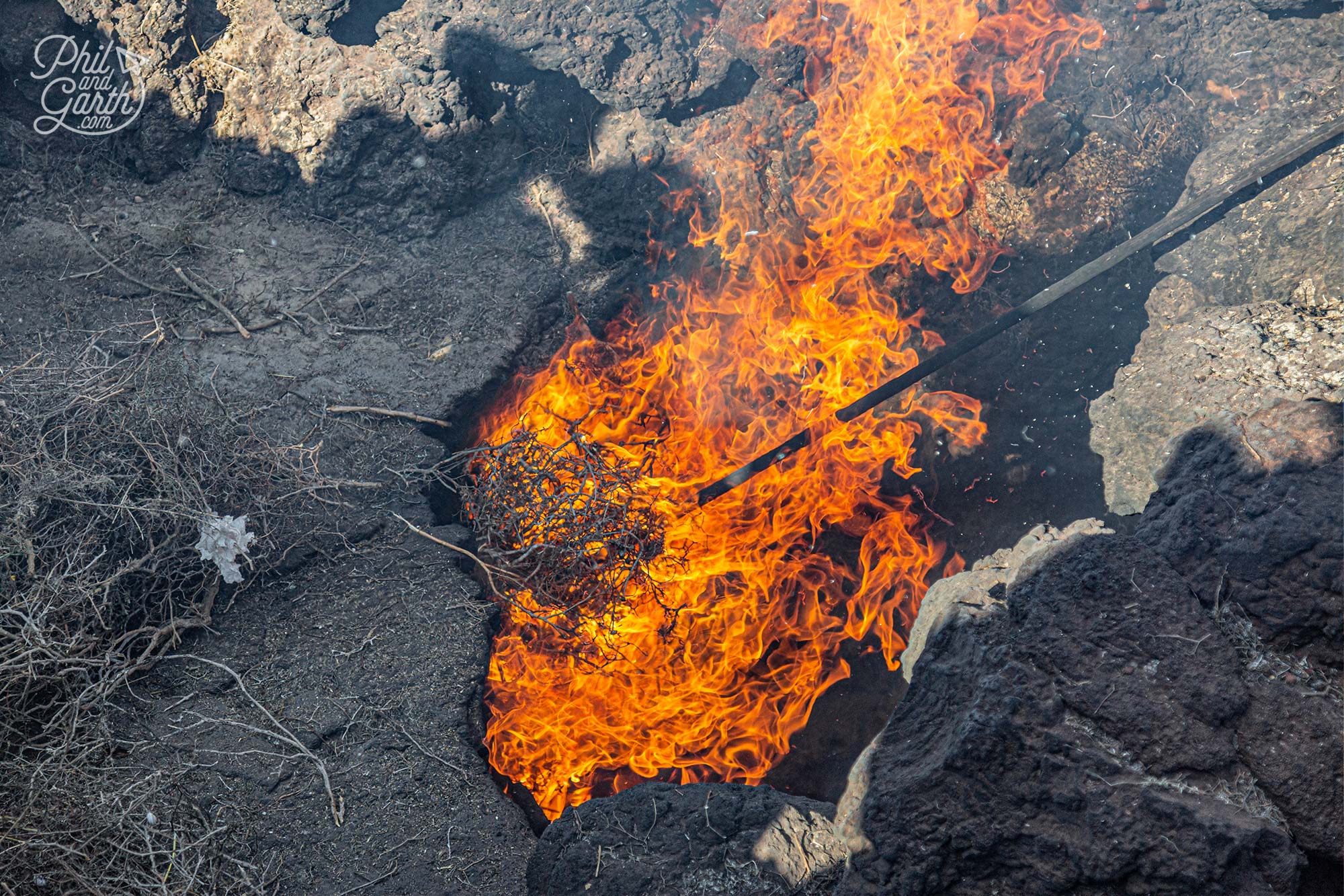 Dry grass is dropped into a shallow pit and quickly bursts into flames