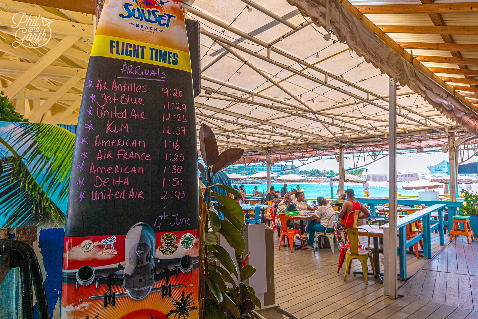 The Sunset Beach Bar posts times of flight arrivals on a surfboard at the entrance