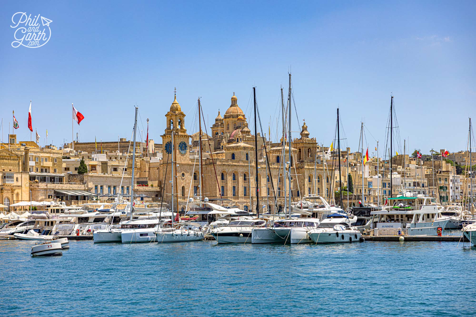 Vittoriosa Marina, with the historic skyline of Birgu rising behind it. The church towers and honey-coloured buildings are classic Birgu